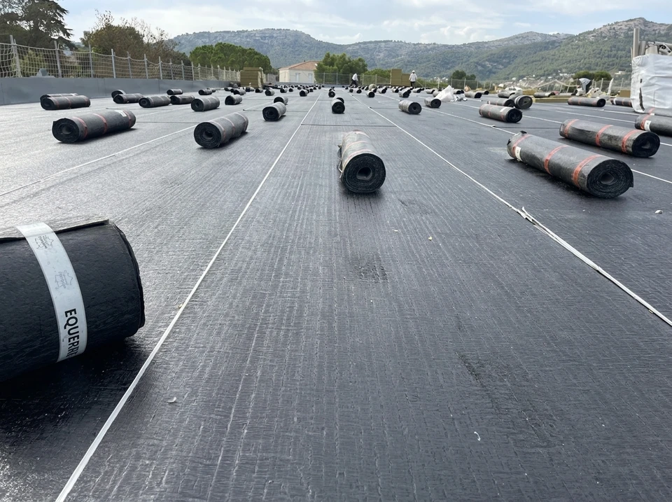Chantier de toiture extérieur avec ouvrier en arrière-plan travaillant sur une couverture